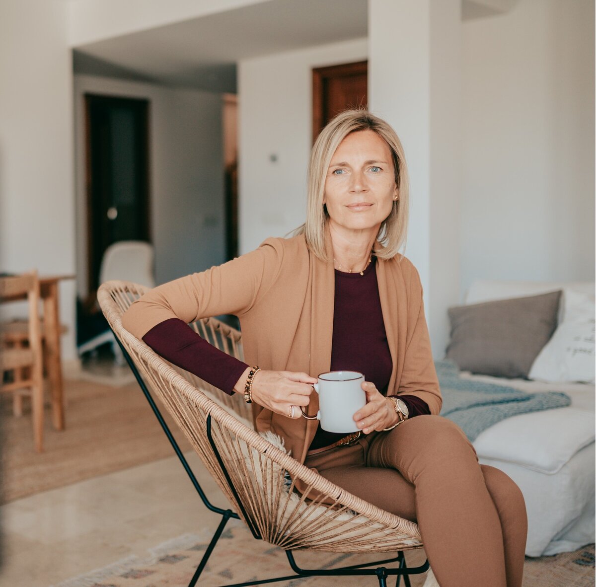 Sylke entspannt mit einer Tasse Tee in einem Korbstuhl sitzend und aus dem Fenster schauend