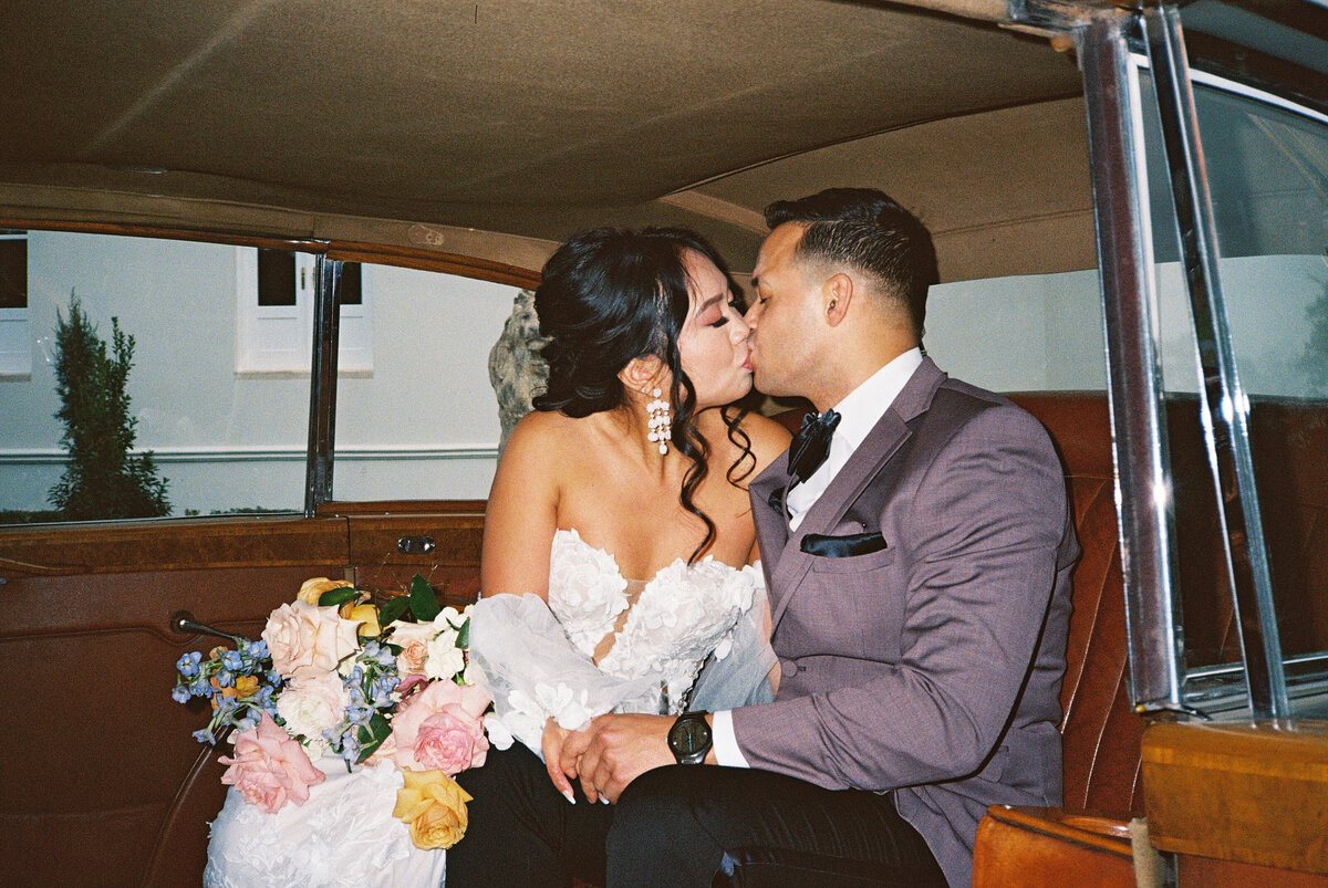 bride and groom garden party bouquet on wedding day kissing in getaway car