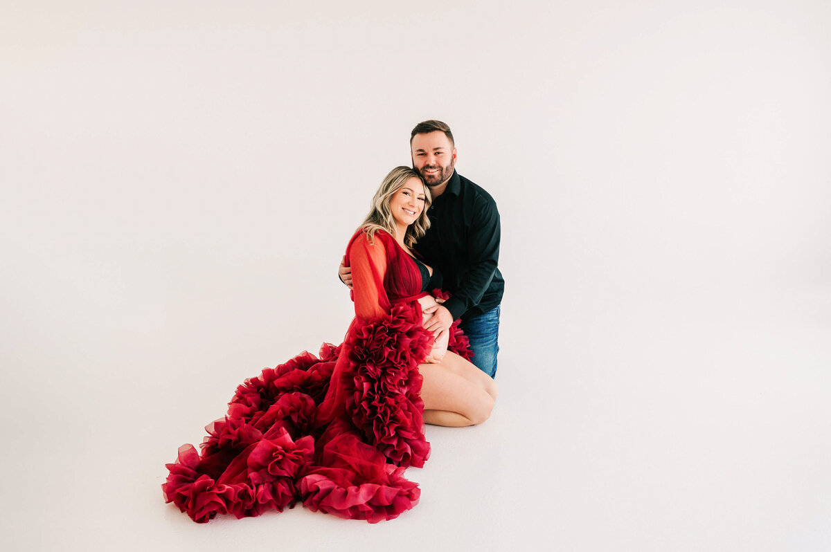 pregnant couple kneeling on floor cuddling in maternity photography studio in Springfield MO