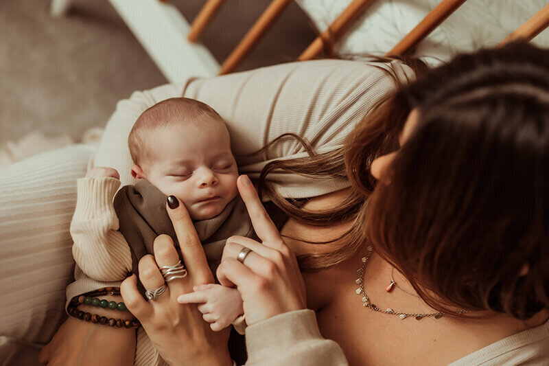 Mom and dad rubbing newborn baby boy's cheek while sleeping in mom's arms