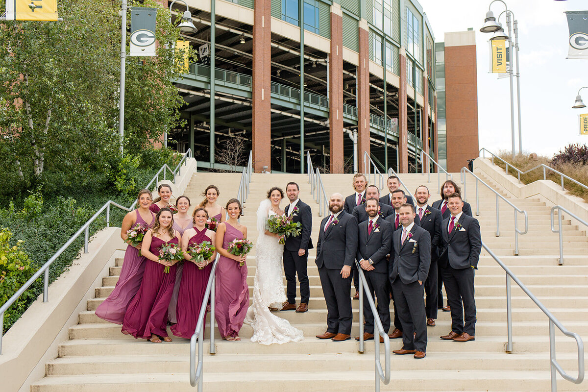 Wedding party photos on stairs outside of Lambeau Field maroon bridesmaid dresses