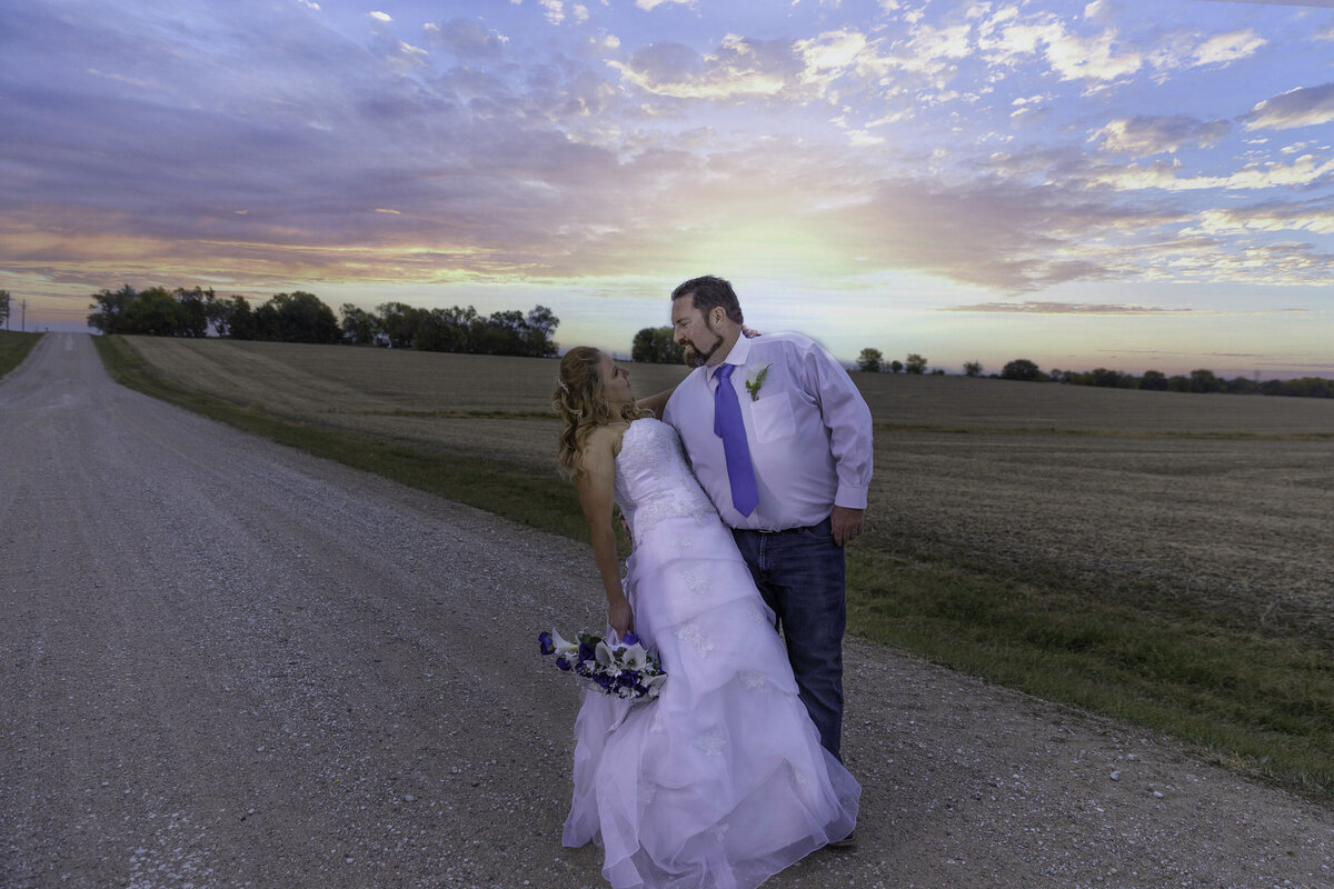 Groom dips bride on a country road with the sun setting