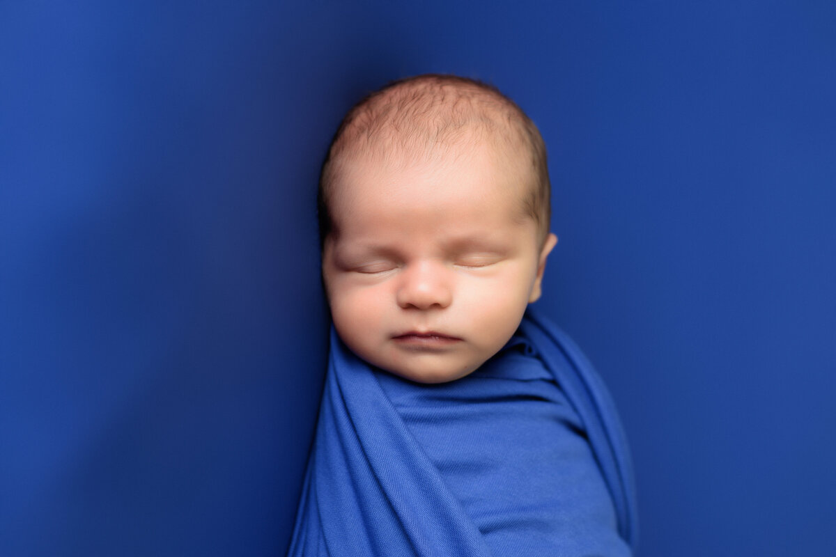 Newborn Photographer, a banby wrapped in blue sleeps on blue bedsheets