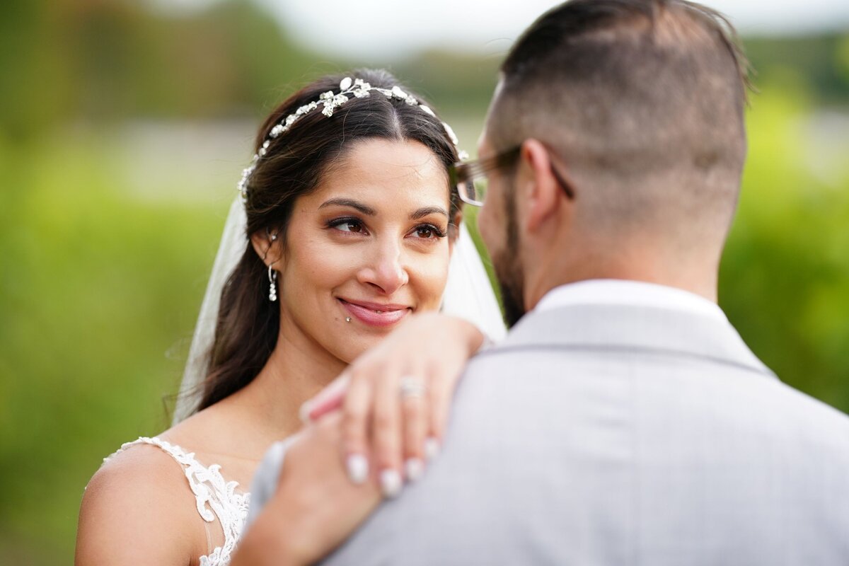 A close-up of the bride smiling warmly at the groom, highlighting their intimate and joyful moment. The image captures the bride’s radiant expression and the deep affection between the couple, emphasizing their connection and happiness on their special day.