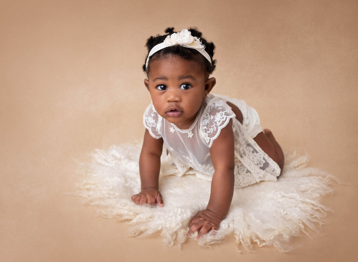 Baby girl crawling during her 6-month milestone photoshoot, wearing a white lace romper and smiling at her NYC baby photographer