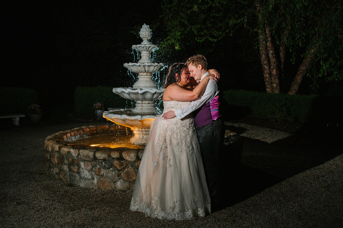 Brides holding each other in front of a water fountain