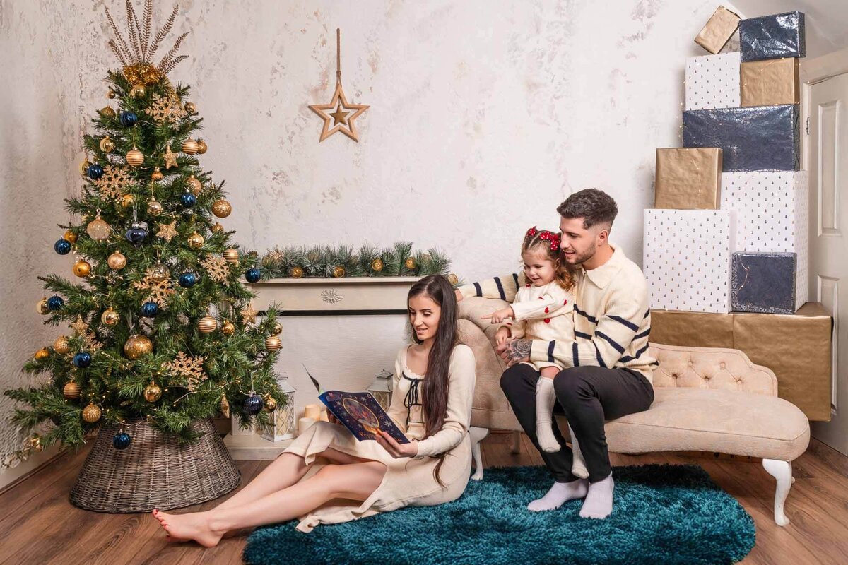 Family reading Christmas story by the tree in Calini Weddings Studio - cozy festive setting with gifts and warm tones.