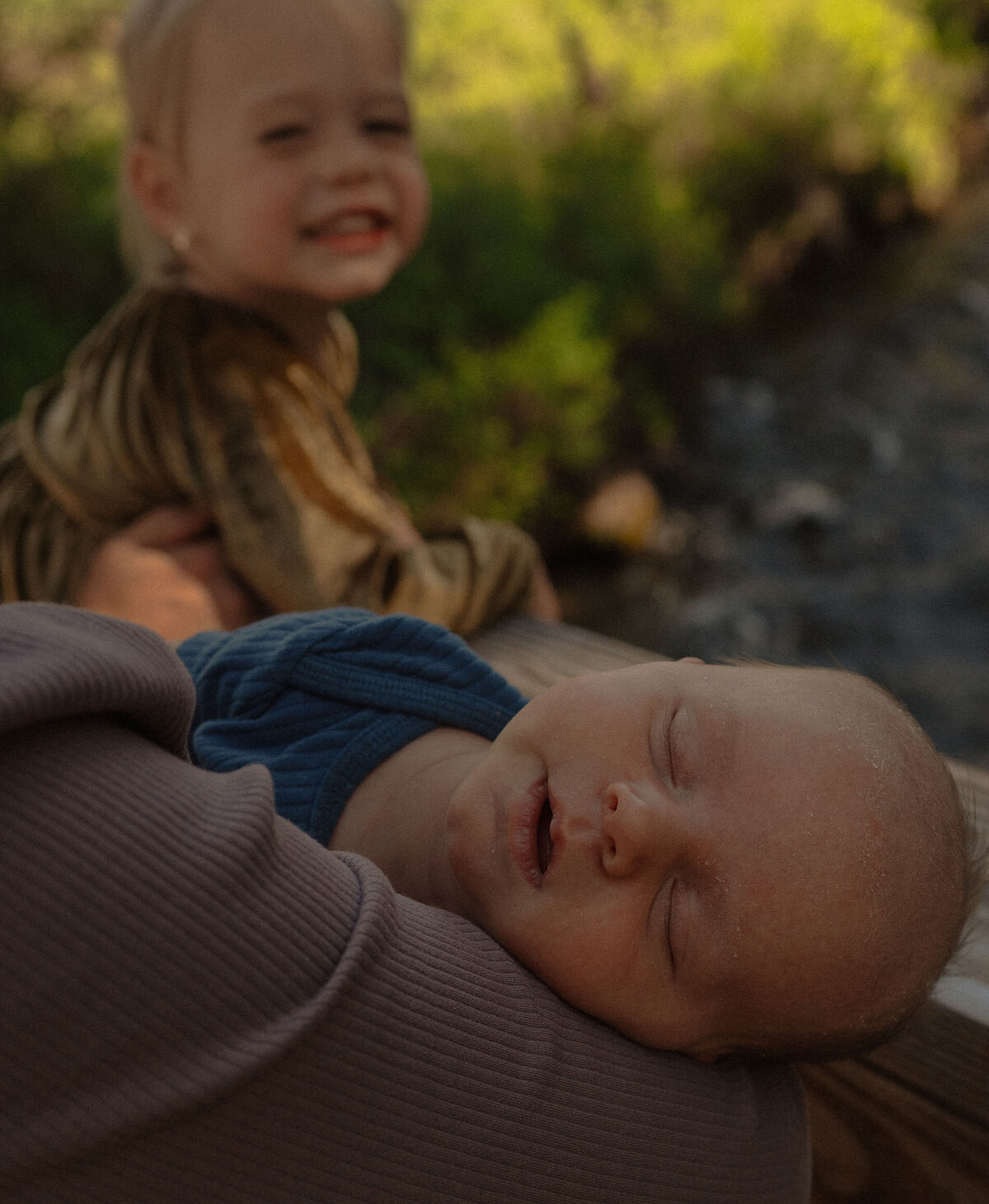 newborn baby sleeping peacefully with mom and big sister nearby during outdoor photoshoot in Bend, Oregon