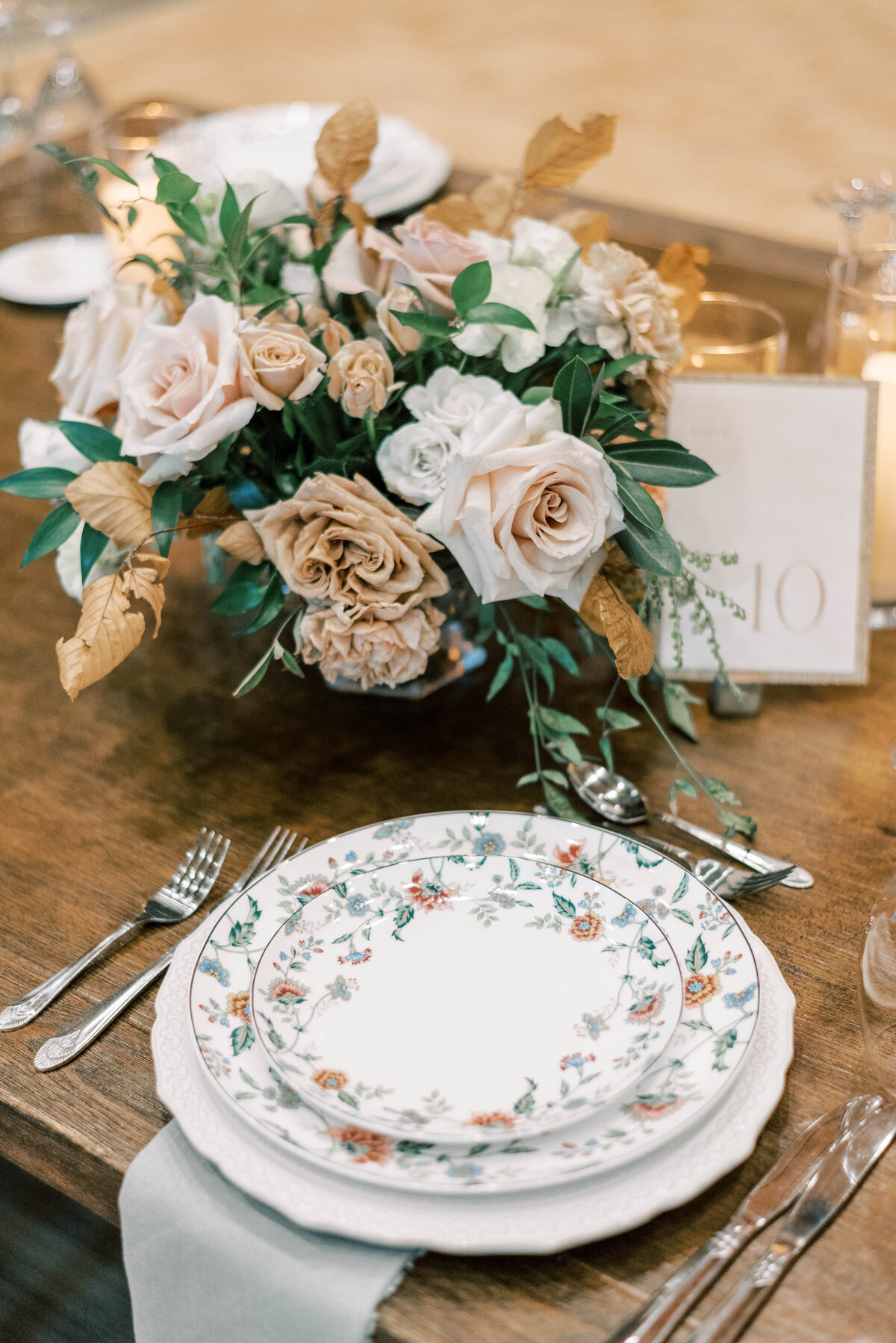 Wedding reception table setting on wooden tables with floral dinnerware and neutral colored floral centerpieces