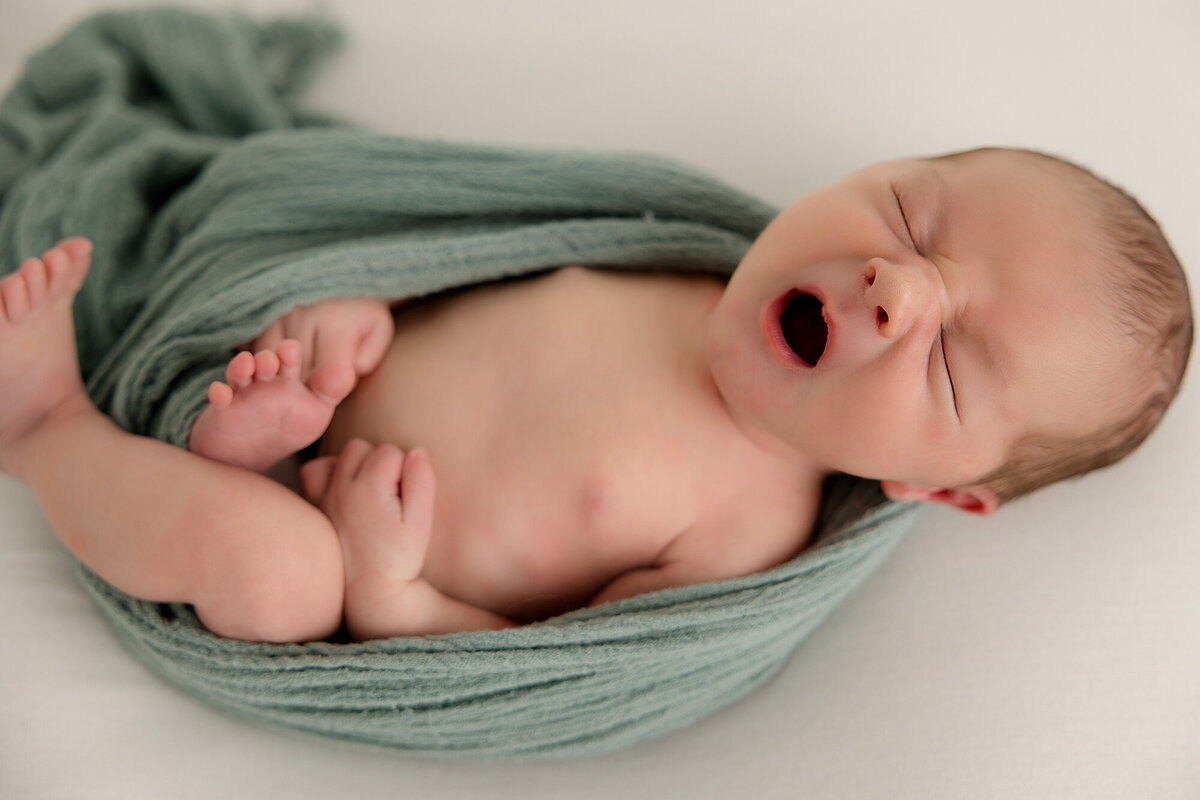 newborn baby boy wrapped in a green swaddle while yawning