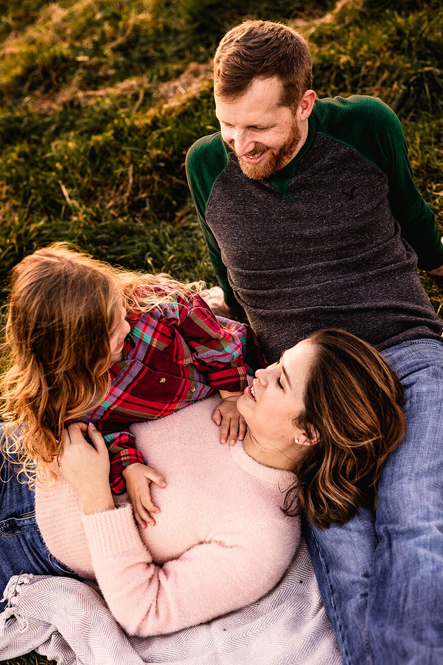 Mom with head in dads lap  while little girl tickles mom at family photo session at Wagon Hill in Durham NH by Lisa Smith Photography