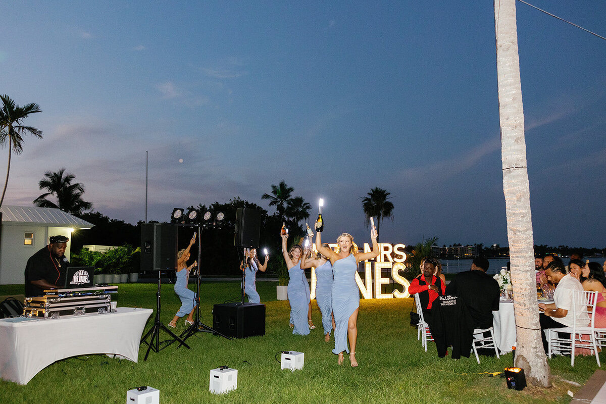 Andressa’s bridesmaids make a lively entrance, celebrating with champagne and sparklers against the glowing “Mr. & Mrs. Jones” sign at the Islamorada wedding reception. Captured by Claudia Amalia, destination wedding photographer.