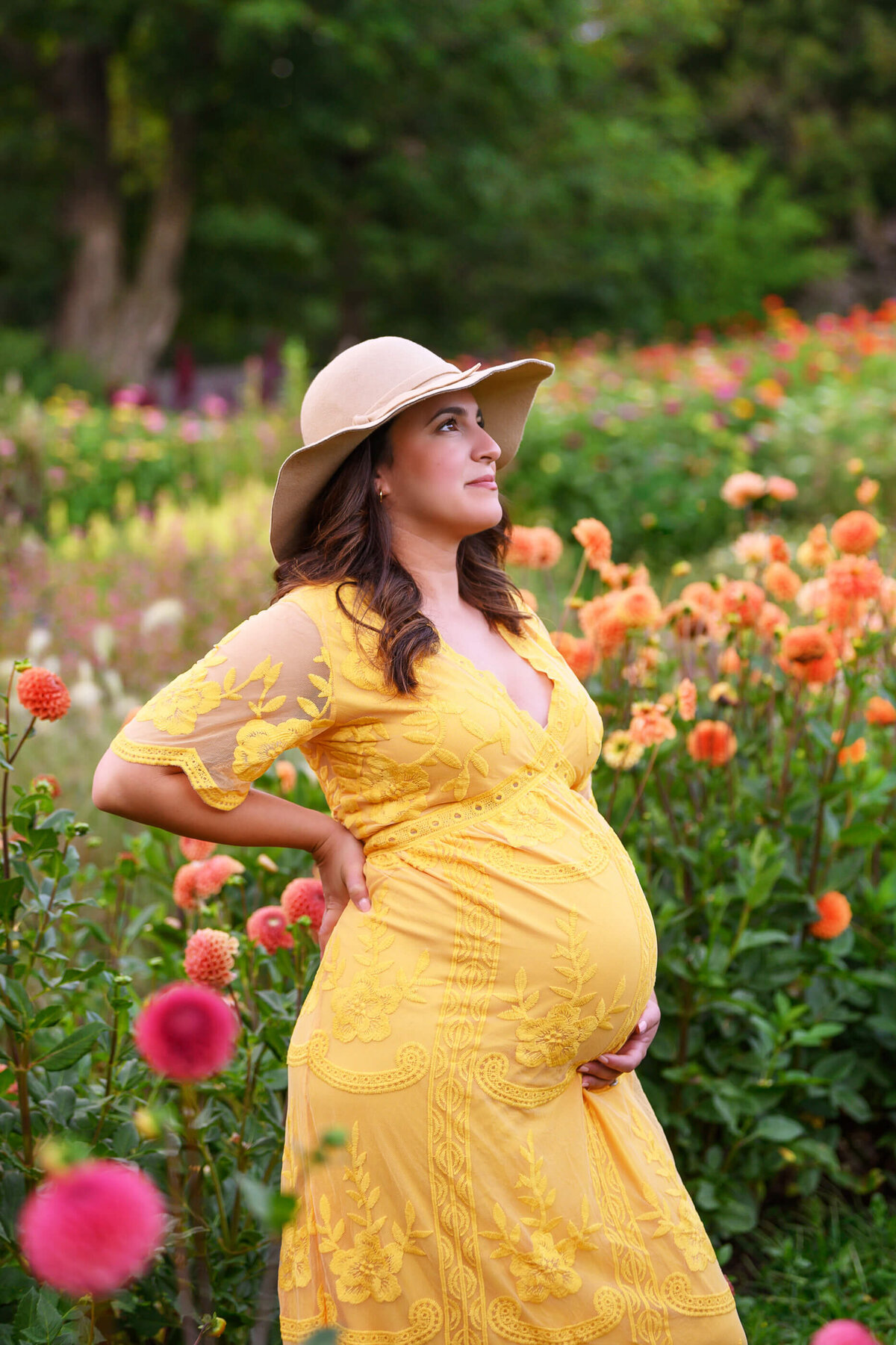 pregnant woman wearing a beige hat and yellow dress for her outdoor maternity photos in the summer.