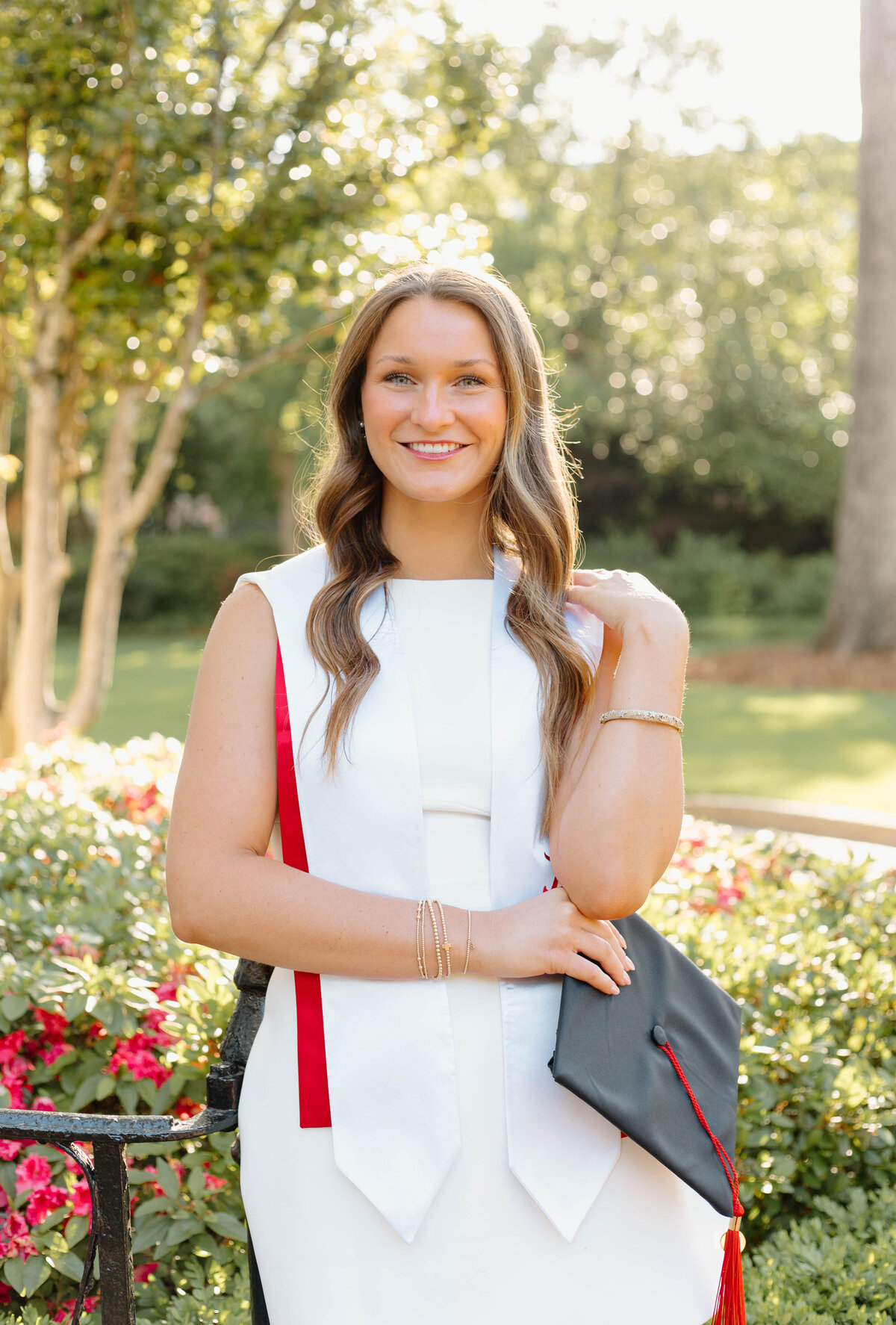 UA graduate wearing stoles and posed in front of the greenery on campus
