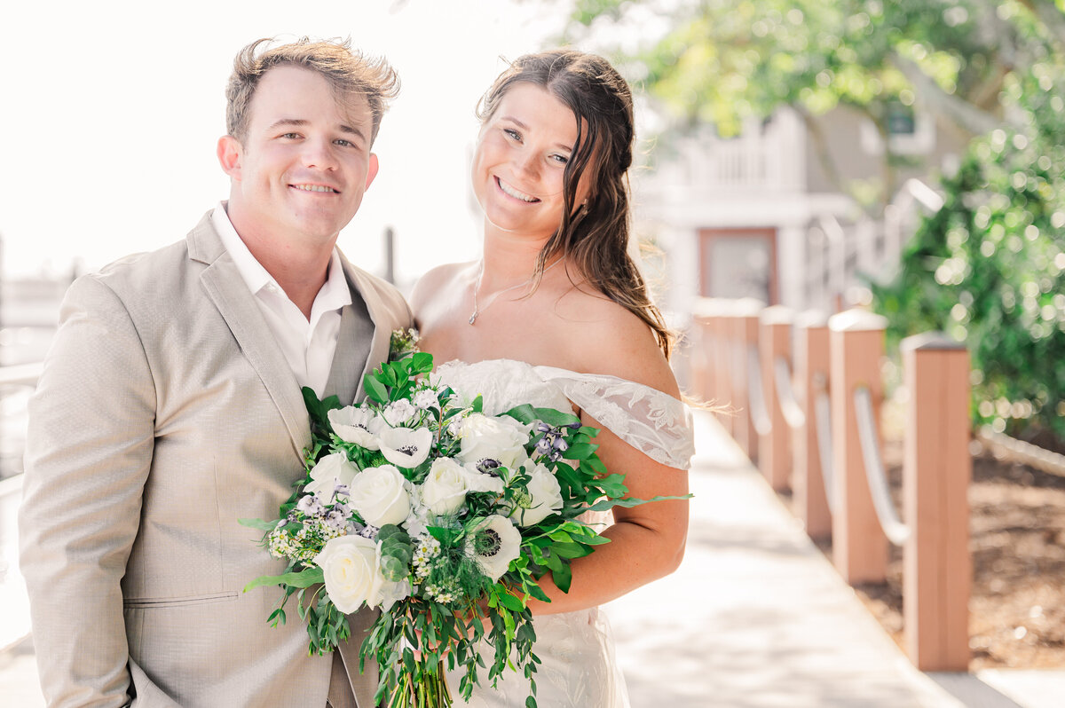 A happy couple smiling on the Wilmington boardwalk during their summer destination wedding by JoLynn Photography