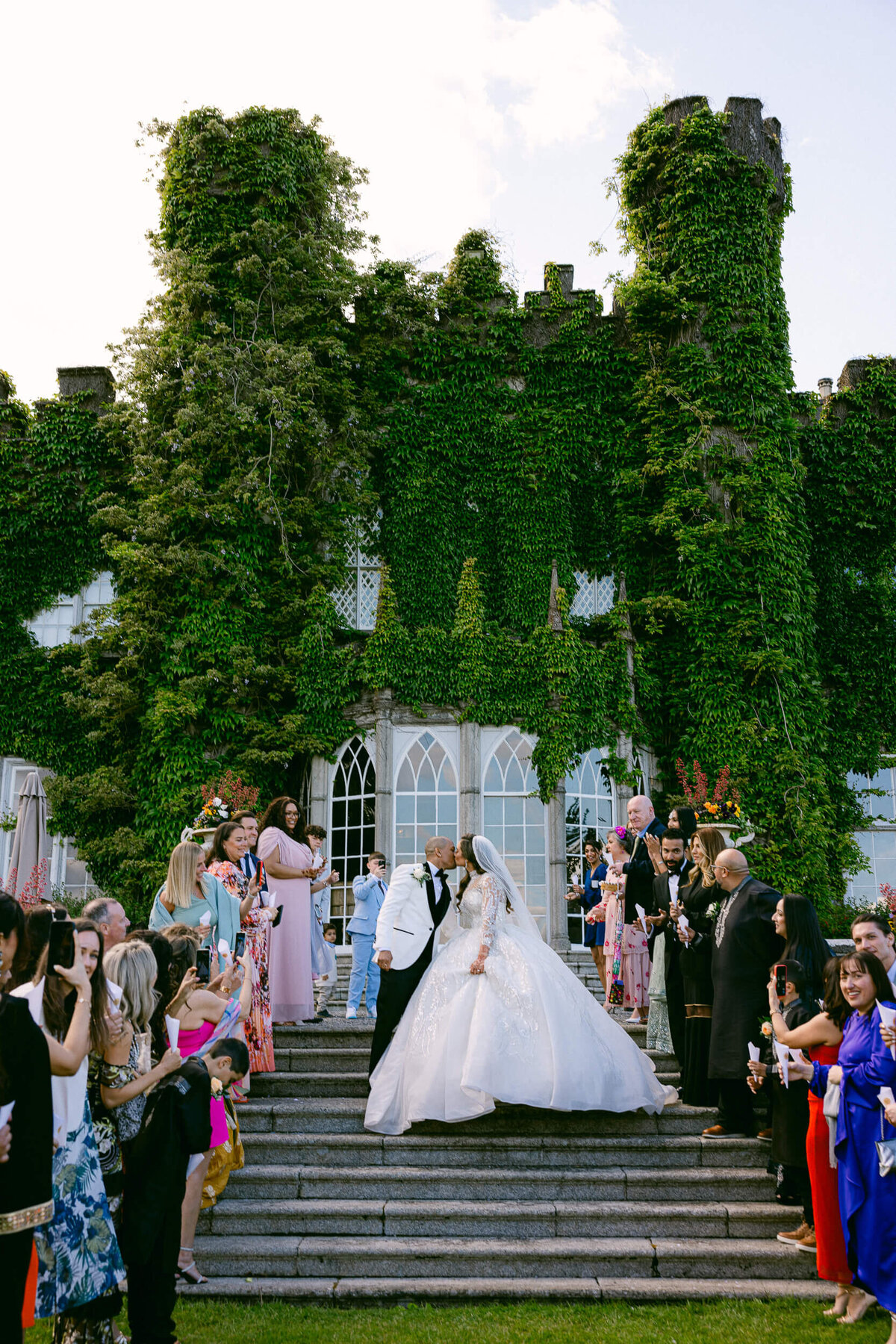 a wedding photo showing the couple kissing with Luttrellstown Castle in Ireland behind them.