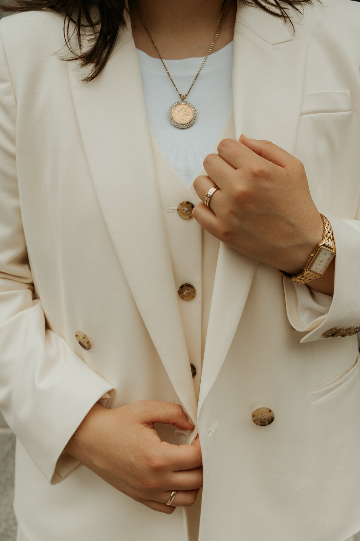 Close-up of a same-sex bride in a stylish cream suit with a gold pendant necklace, wedding ring, and elegant wristwatch. Ideal for couples seeking a documentary wedding photographer who captures unique and sophisticated bridal details with an artistic touch.