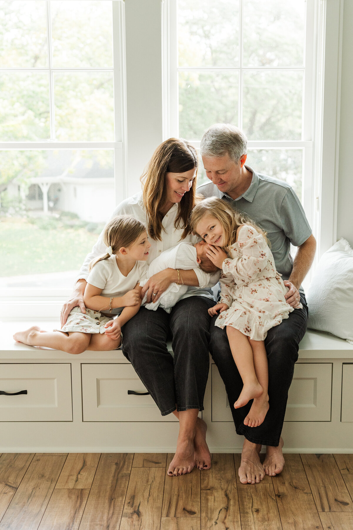 A family of five sitting together, smiling and enjoying a joyful moment with their newborn baby
