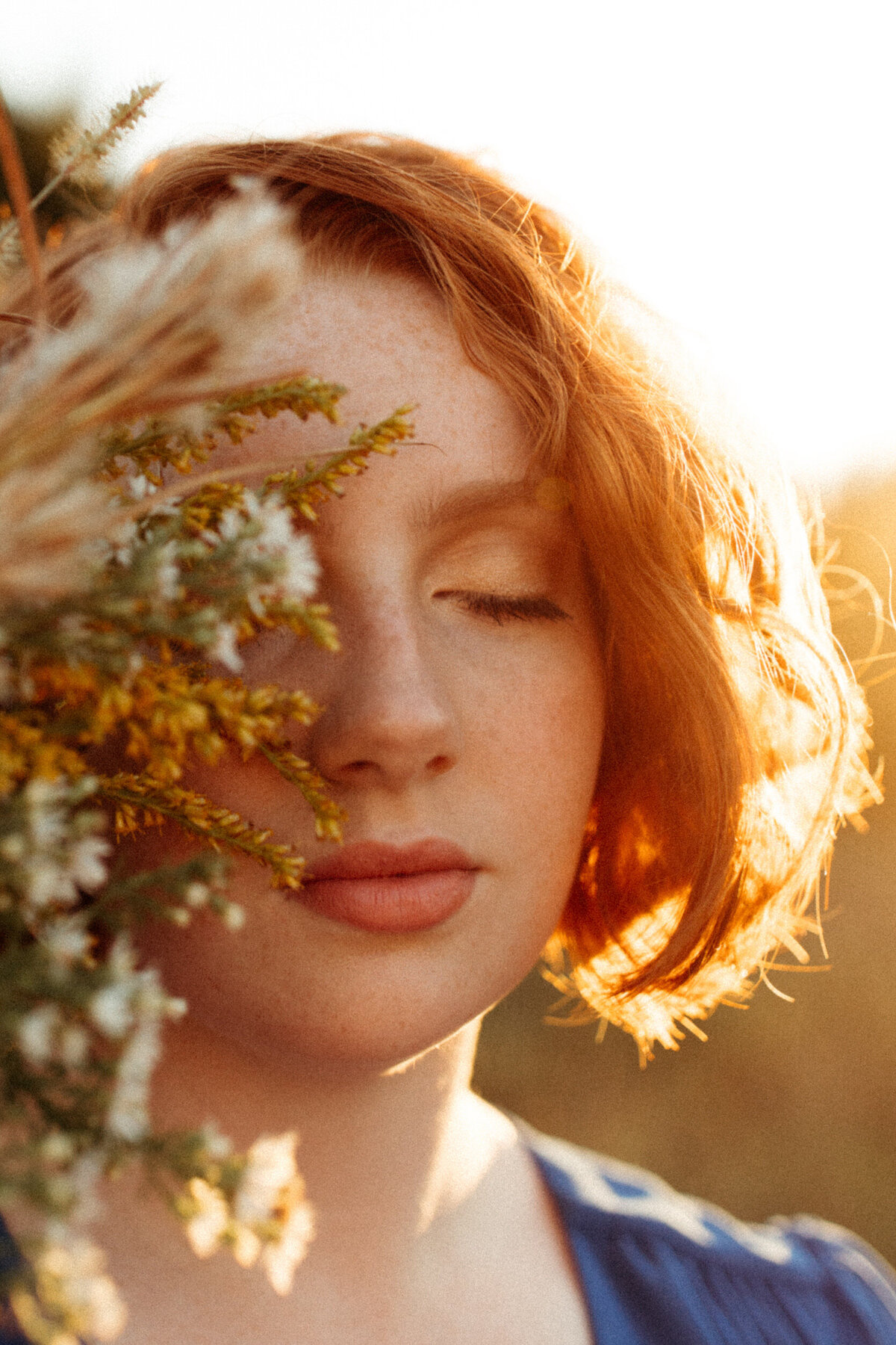 Senior with red hair holding wildflowers over half of her face at golden hour