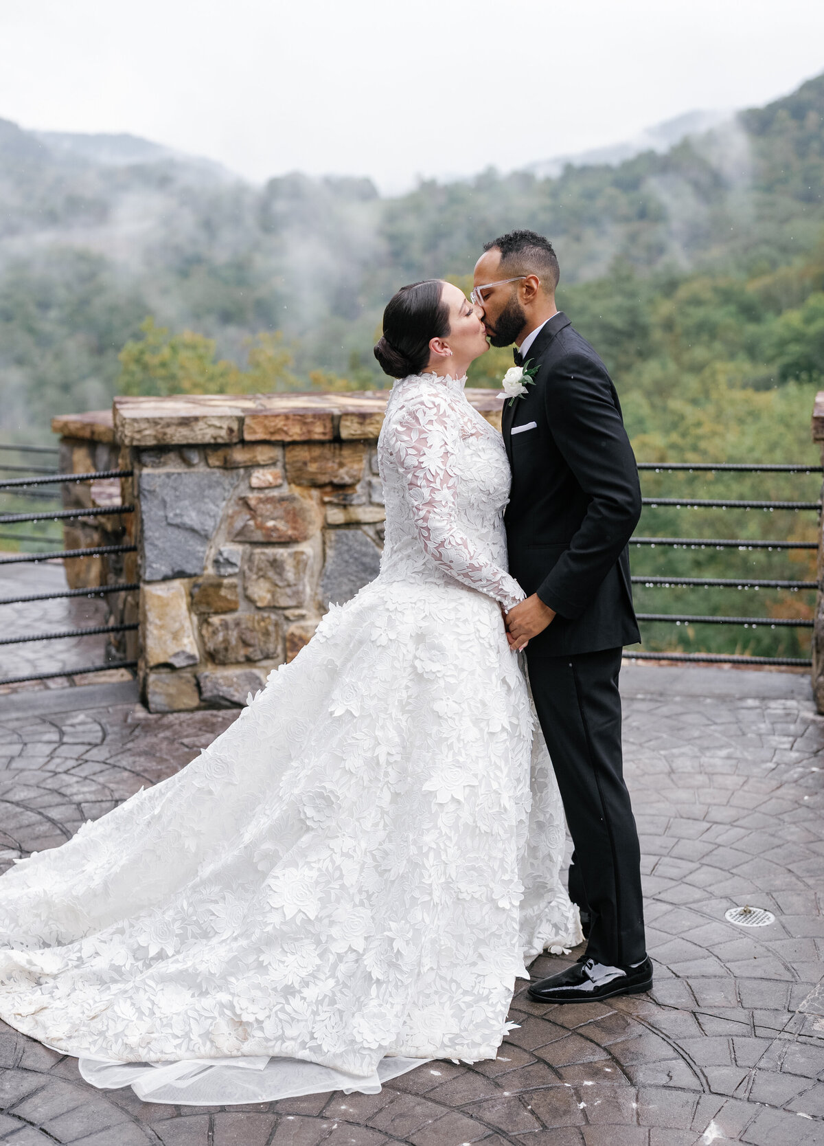 Bride and groom sharing a kiss on the scenic overlook terrace at Castle Ladyhawke with misty mountains behind them.