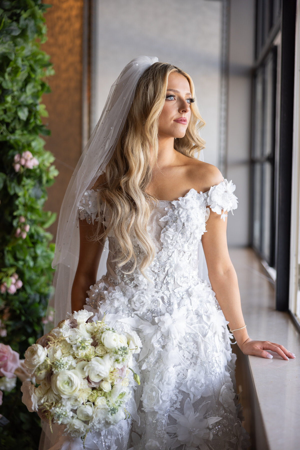 A bride looking out a window and holding a bouquet of flowers