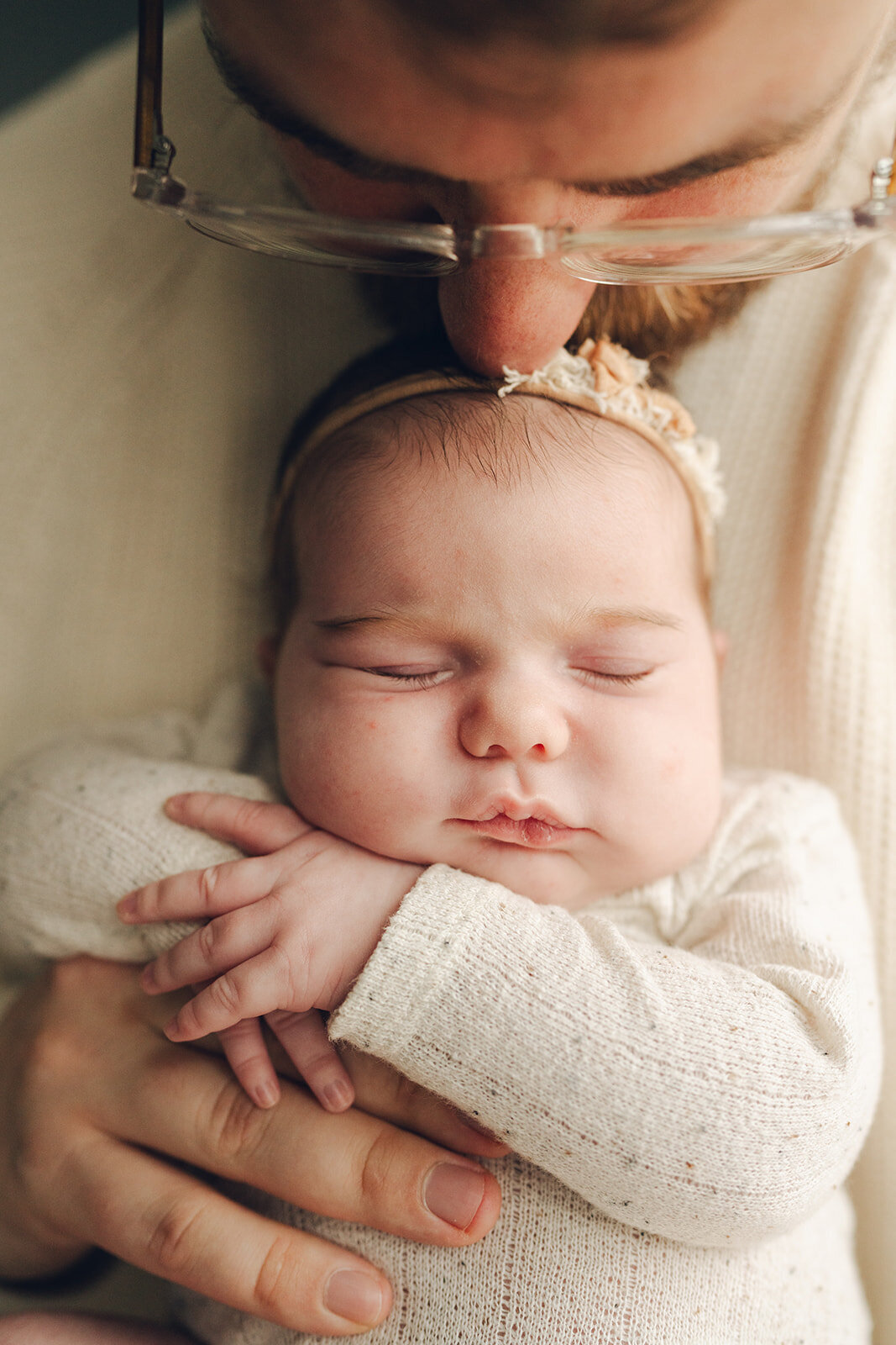 Tiny newborn girl resting safely in her father’s hands during an in-home newborn session