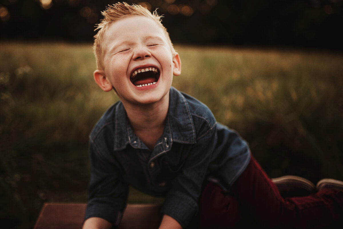 A young boy loudly laughed while lying on a wooden bench.