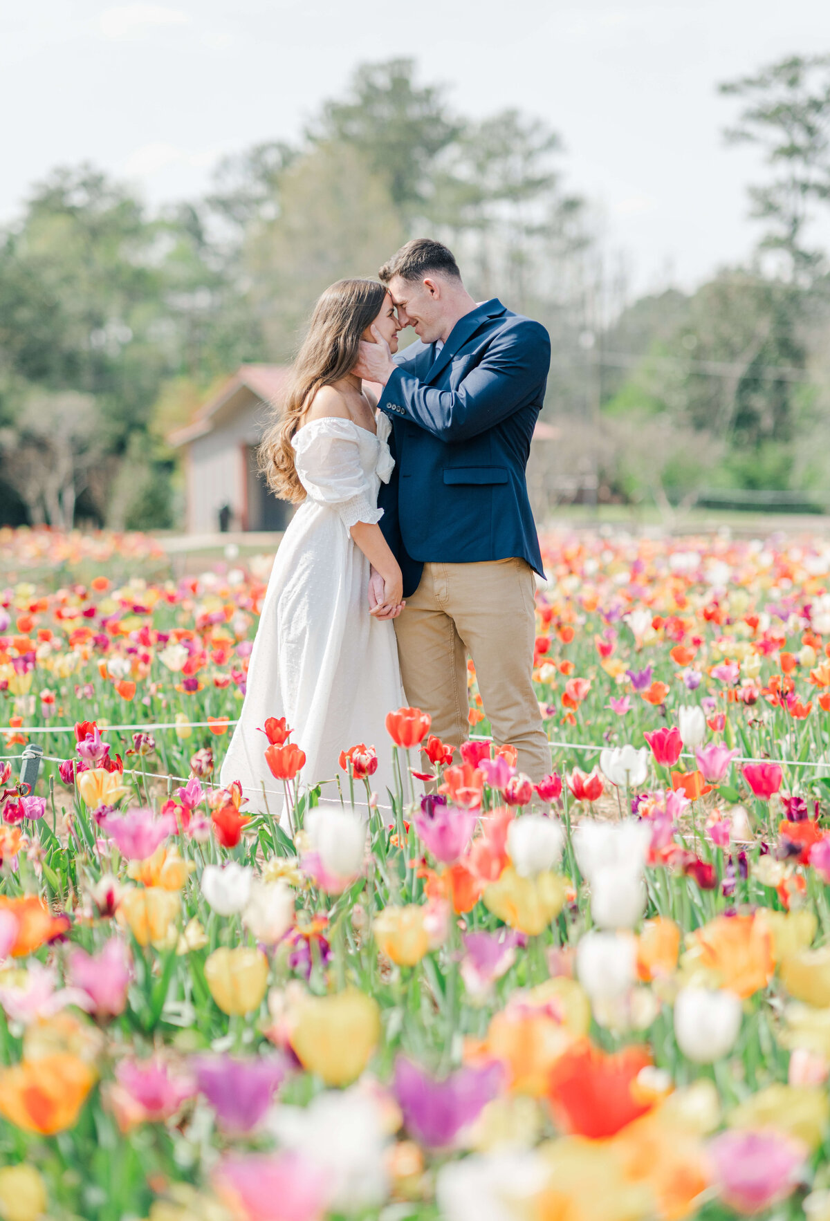 Couple standing in a field of colorful tulips while they hold hands and smile at each other