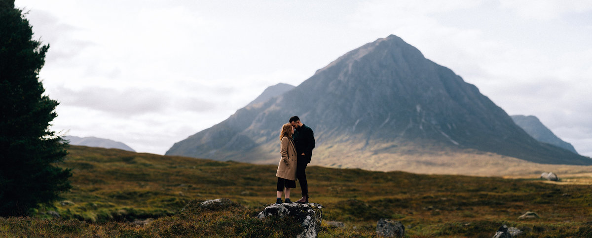 Engaged couple standing lovingly under the mountains in Glencoe Scotland