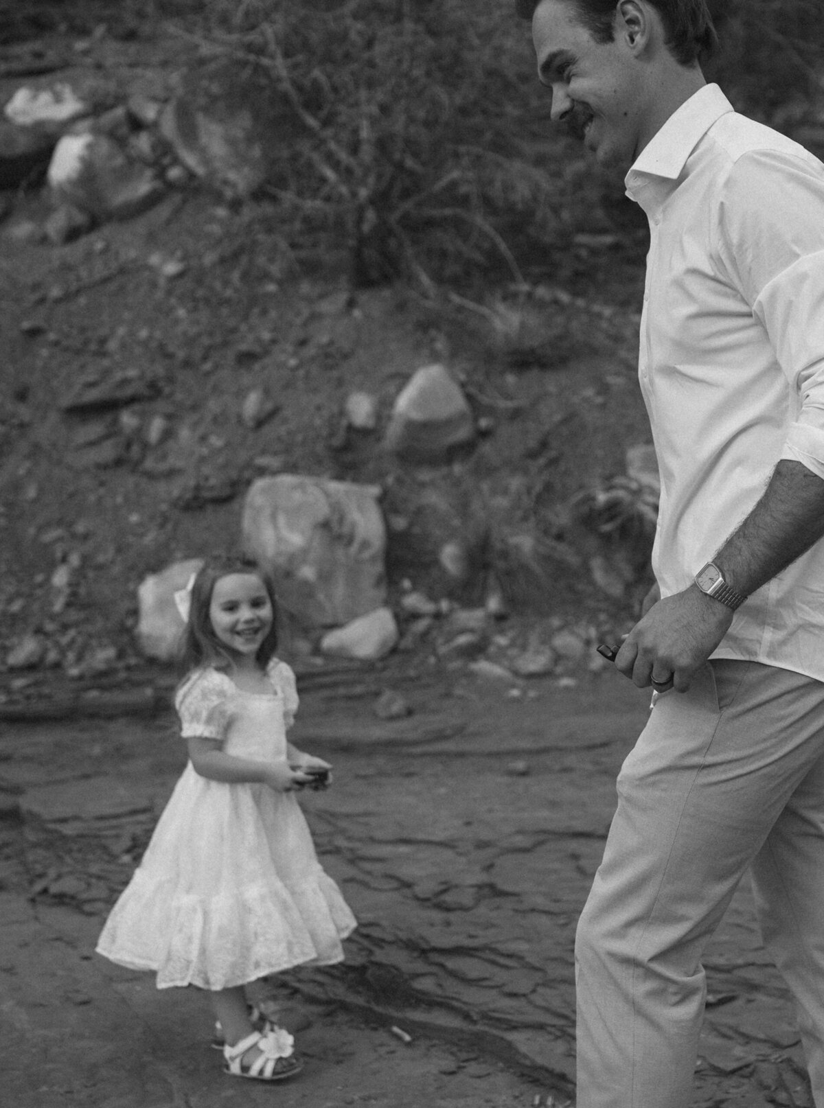 a young girl in a white dress stands next to the groom in the Moab desert during an elopement