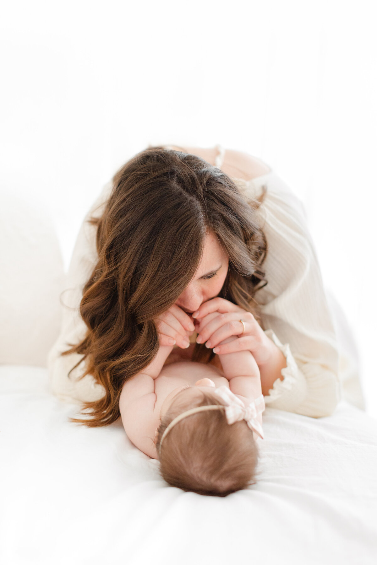 A Baby Photography photo in Northern Virginia of a  mother kissing her daughter's hands on a white bed