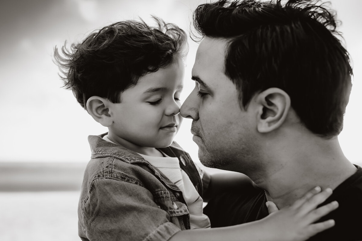 black and white beach photo of a son and father doing nose kisses