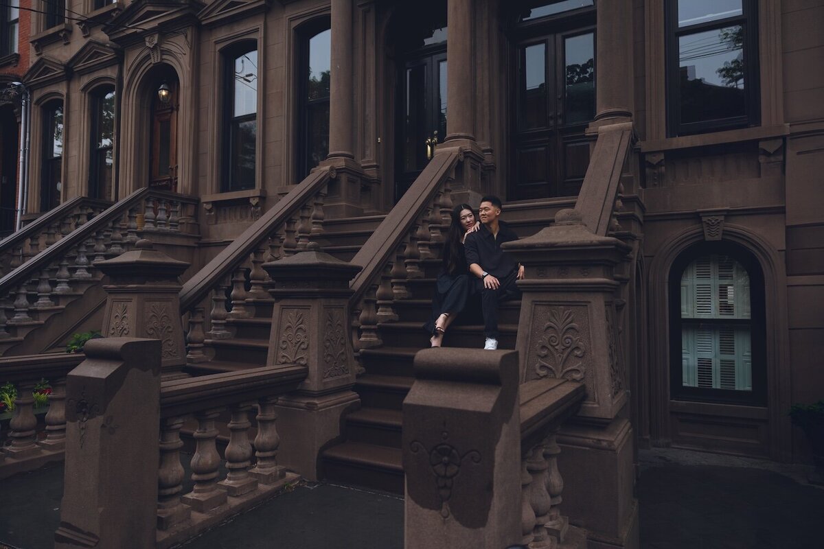 Couple cozying up on brownstone stairs during rainy engagement shoot