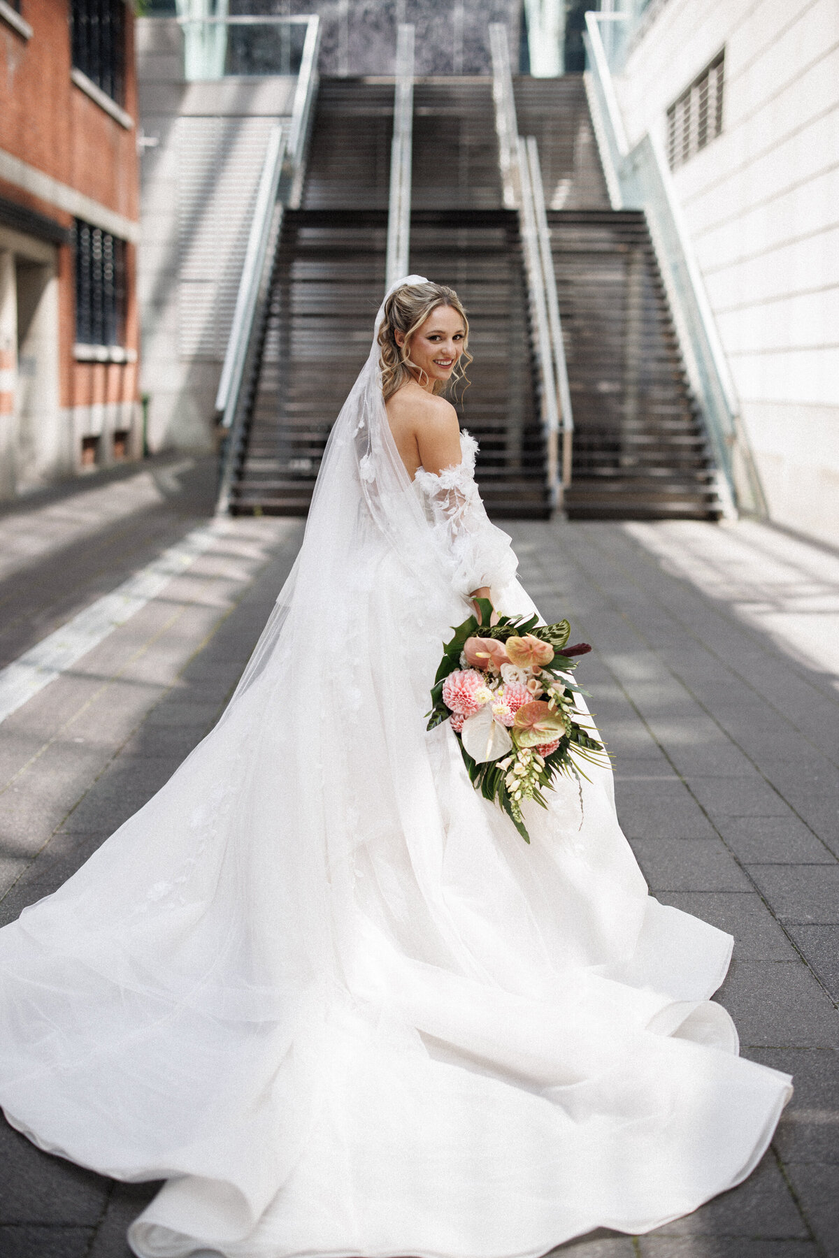 A bride looks over her shoulder in front of the Cathcart, holding an exotic flower bouquet.