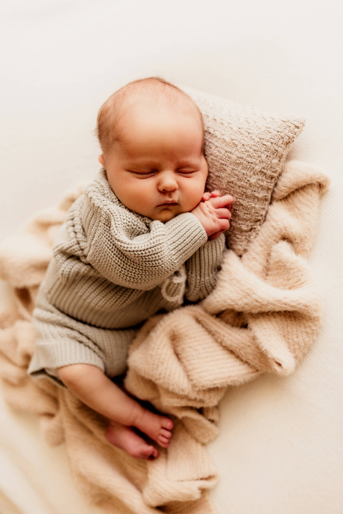 Baby boy posed with his hands by his face on a beige pillow in Oklahoma City.