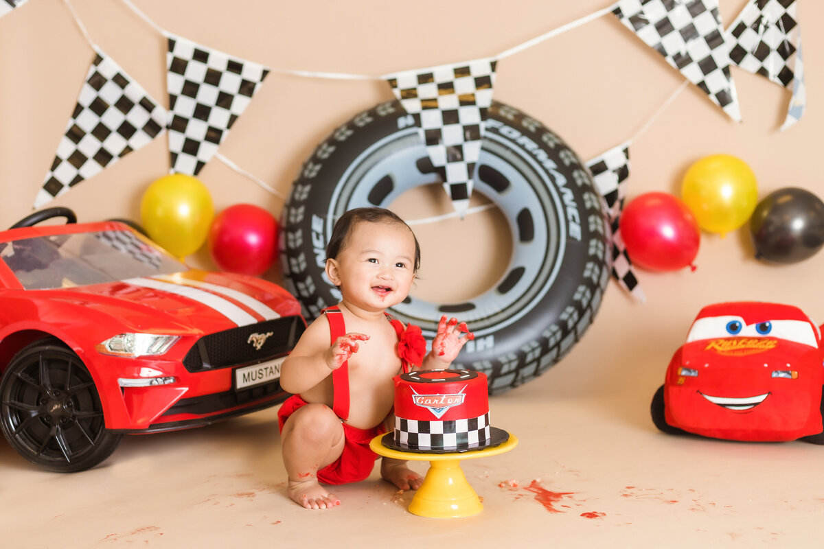 Cake Smash Photographer, a baby boy sits in front of the "Cars" Movie cake and cars