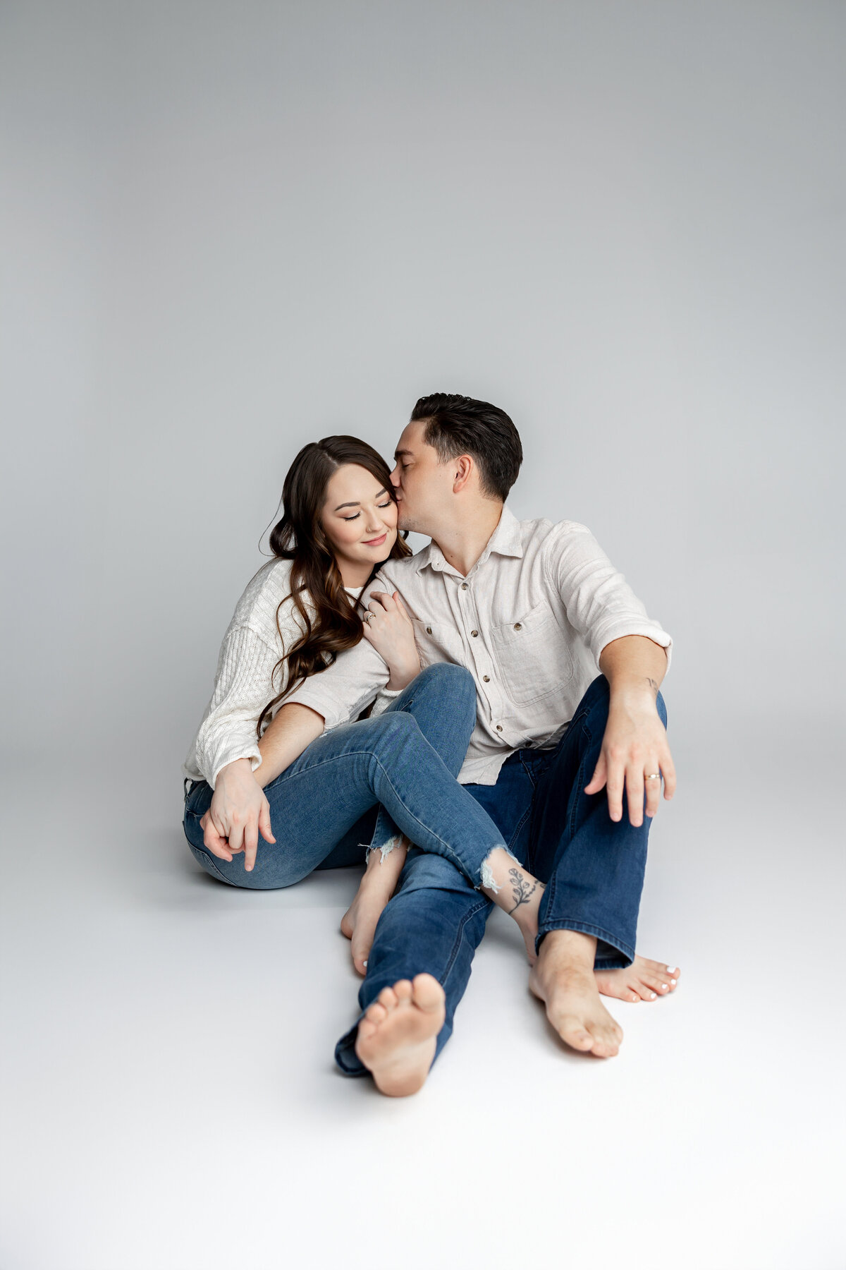 Couple sitting on floor with arms around each other in denim and white outfits. Photographed by Yucaipa family photographer Kaitlyn Dawn Photography.