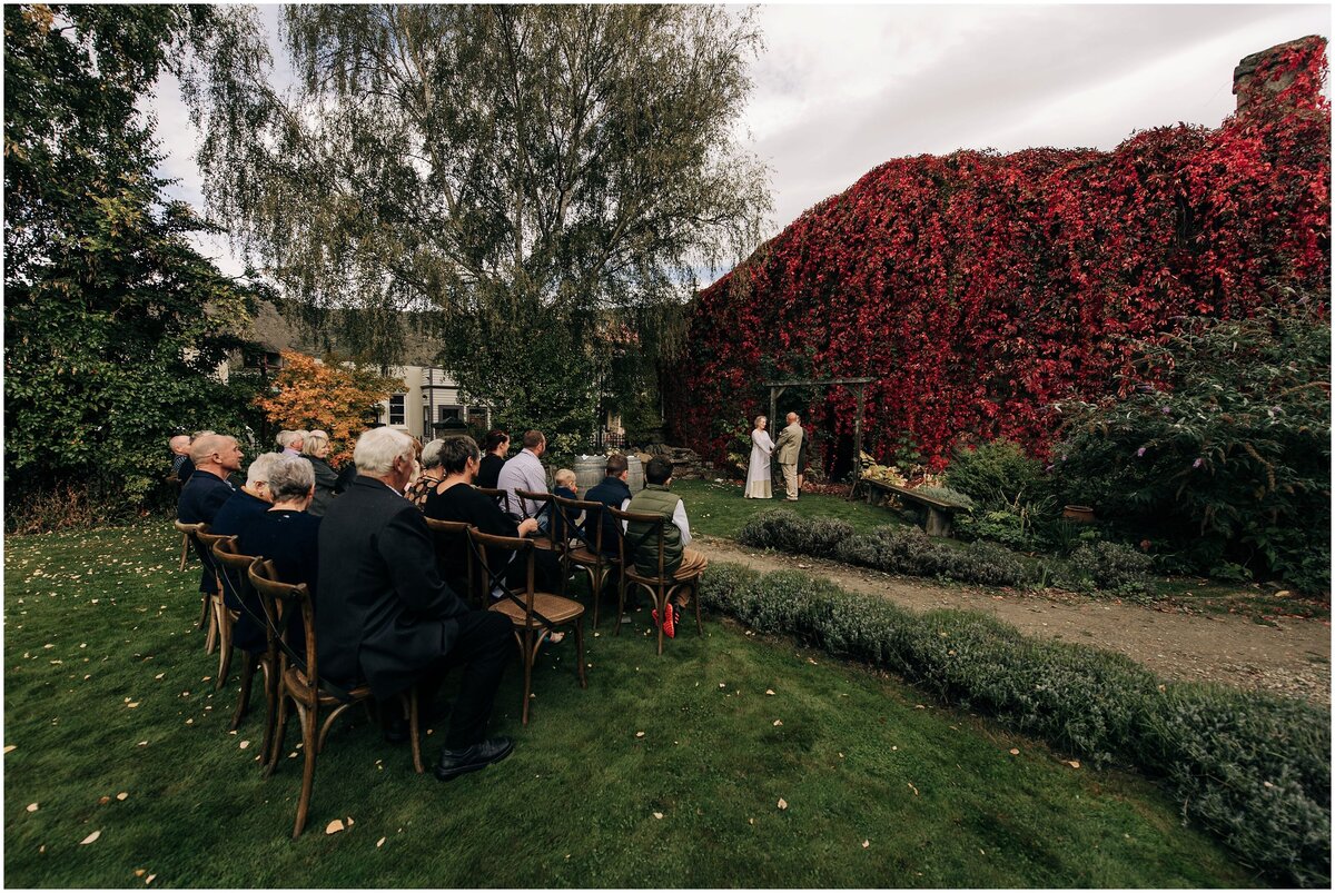 wedding ceremony on lawn at olivers victoria store in clyde with red creeper vine small elopement in new zealand thirty guests