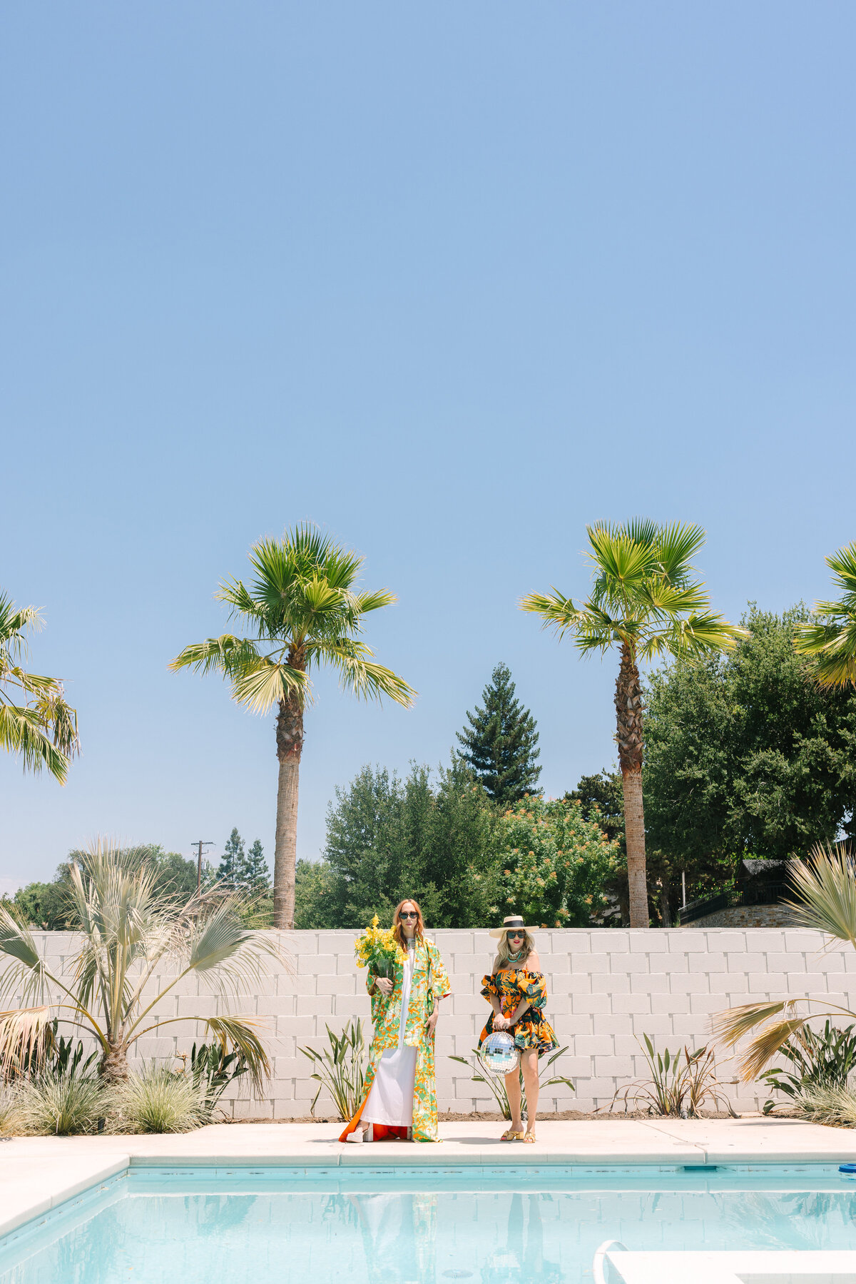 Editorial poolside branding shoot with two women holding florals and disco balls on a sunny day. Greenville SC. Dani Lacey Photographs.