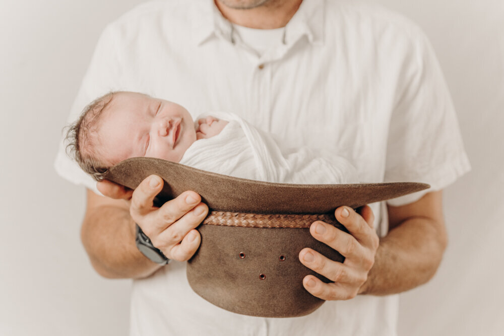 posed newborn baby wrapped and held in a cowboy hat by dad - Townsville Newborn Photography by Jamie Simmons