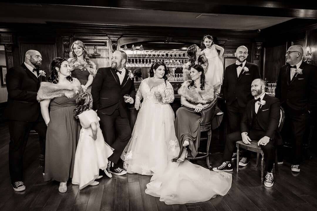 Bride and groom celebrate with their wedding party in an elegant indoor winter wedding reception, captured in classic black and white.