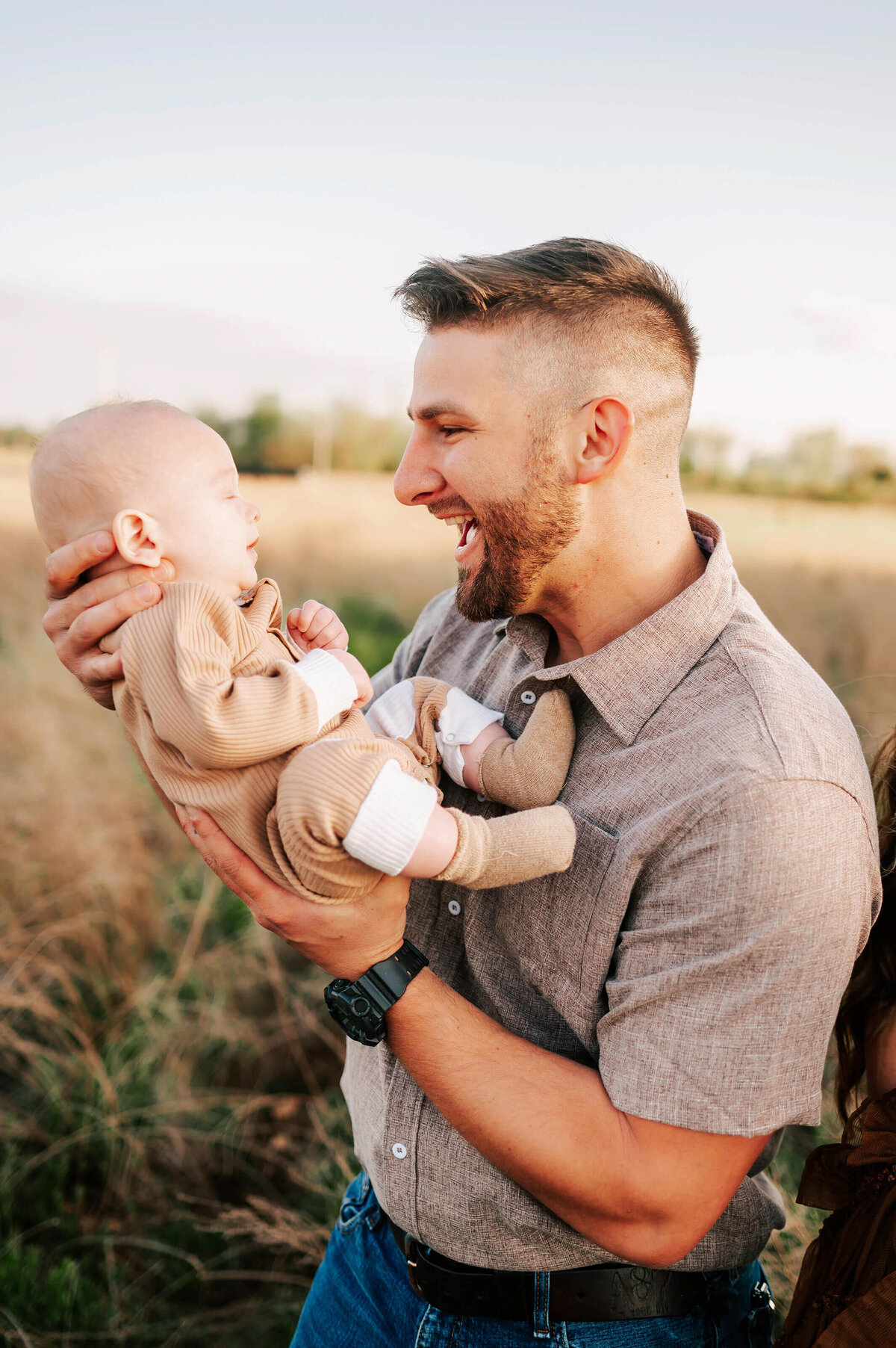 Branson family photo of dad smiling at baby in a field at sunset