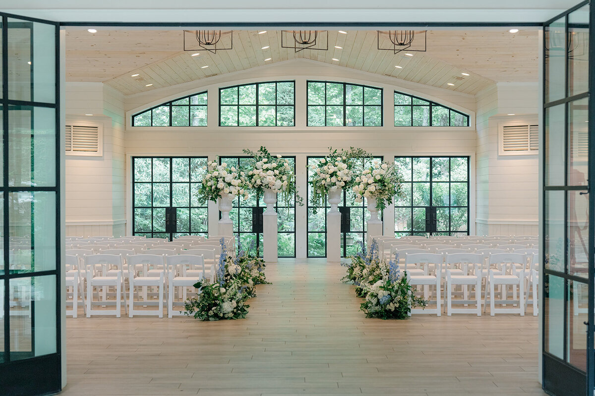 Indoor ceremony setup with tall white floral urns and greenery lining aisle at an elegant Highlands NC wedding venue.