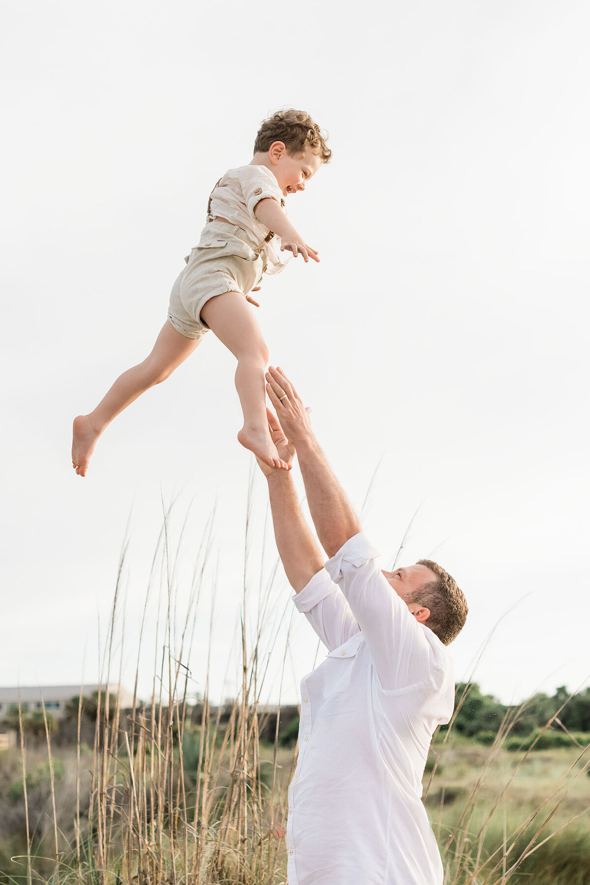a father is tossing his son high up in the air in a beautiful; beach location