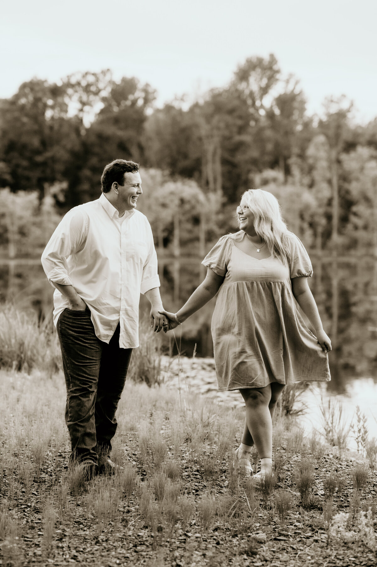 man and woman holds hands and walk along the lake in little rock ar as they smile to each other for their little rock engagement  photos