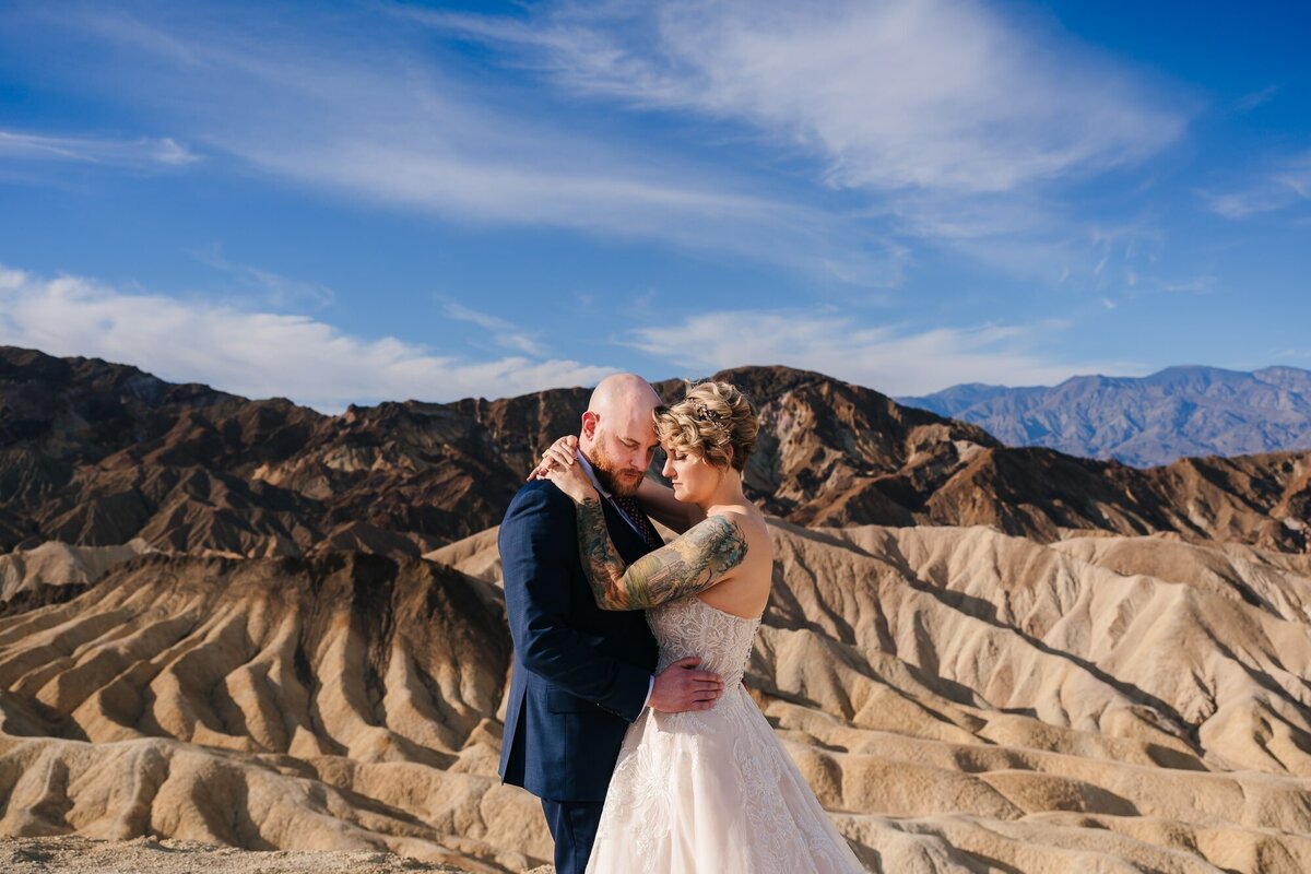 A captivating elopement moment at Zabriskie Point in Death Valley, where the couple shares a tender, face-to-face connection, with the majestic backdrop of nature's beauty enhancing their love story.