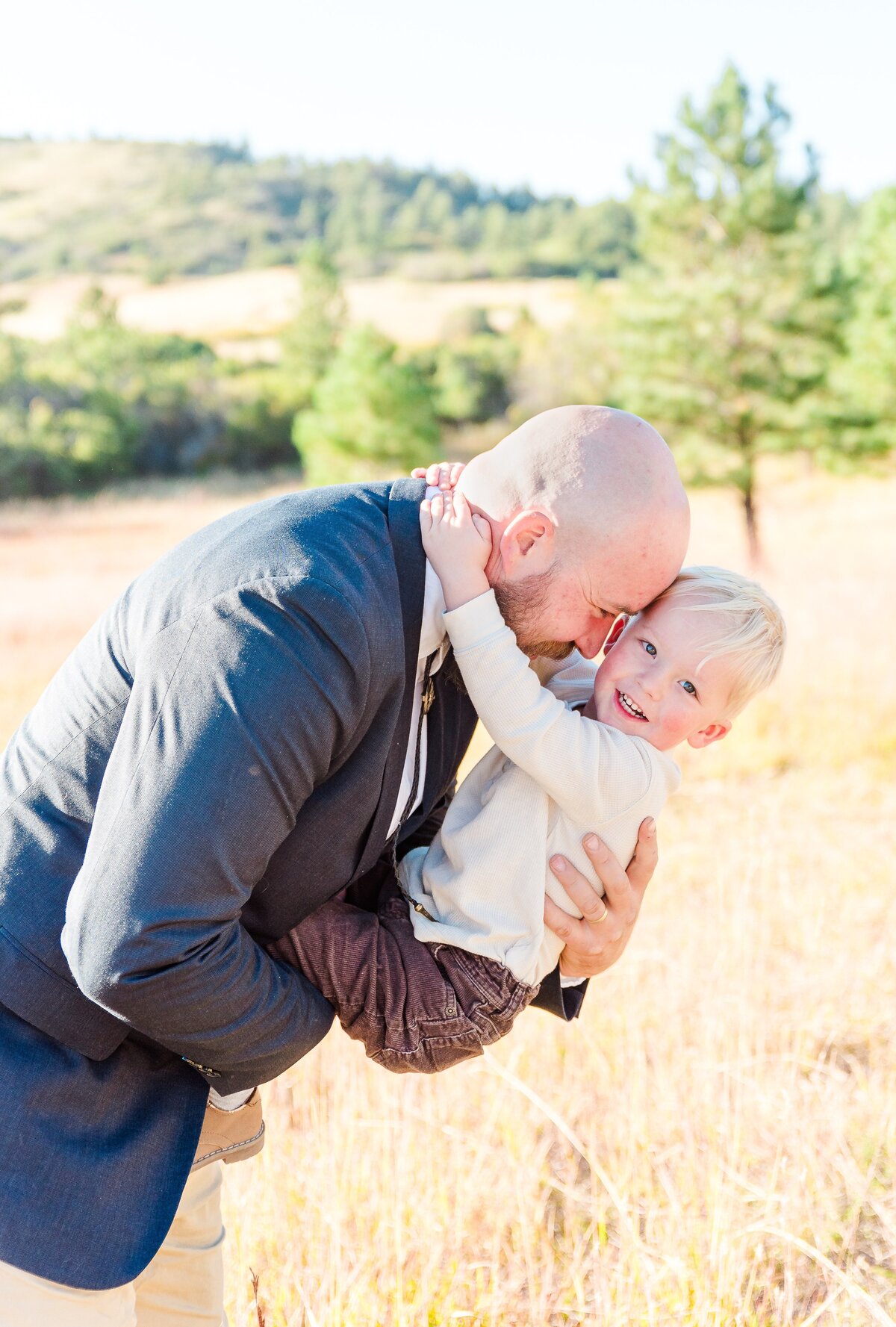 A dad in a blue suit holds his son in front of him and leans forward while holding him