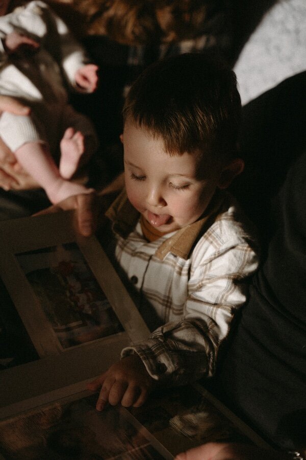 Petit garçon feuilletant un album photo en famille, plongé dans ses découvertes. Photo par Kamescop, vidéo et photographe famille.