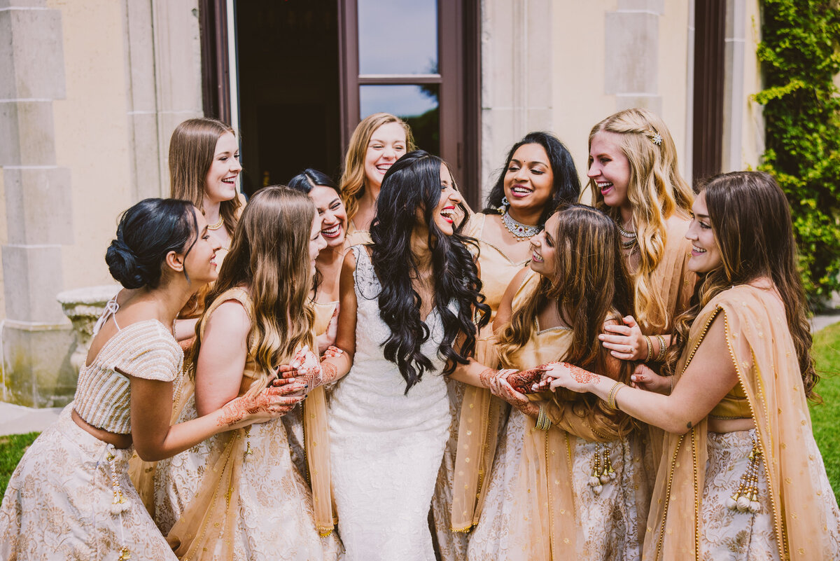 Indian bride in white dress laughing with her bridesmaids at oheka castle
