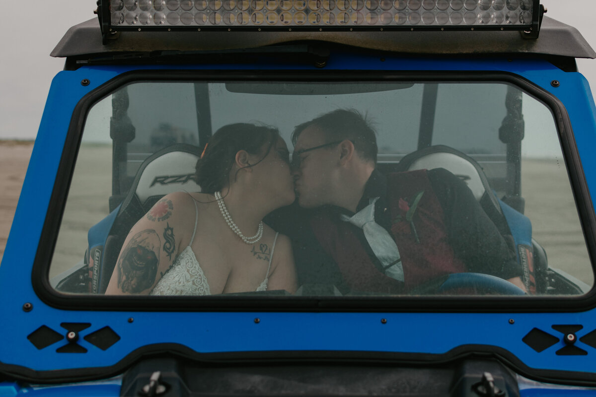 Bride and groom kissing inside a 4-wheeler on the beach.